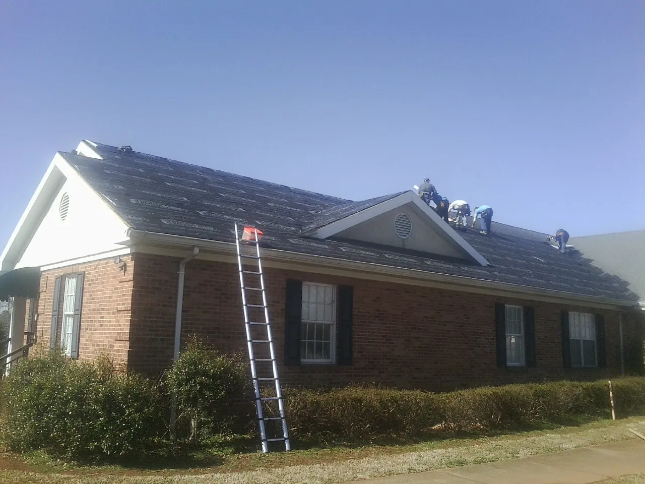 Crew tearing shingles off a brick ranch roof with a ladder set — Metal Roof Repair work by our crew in Rising Sun