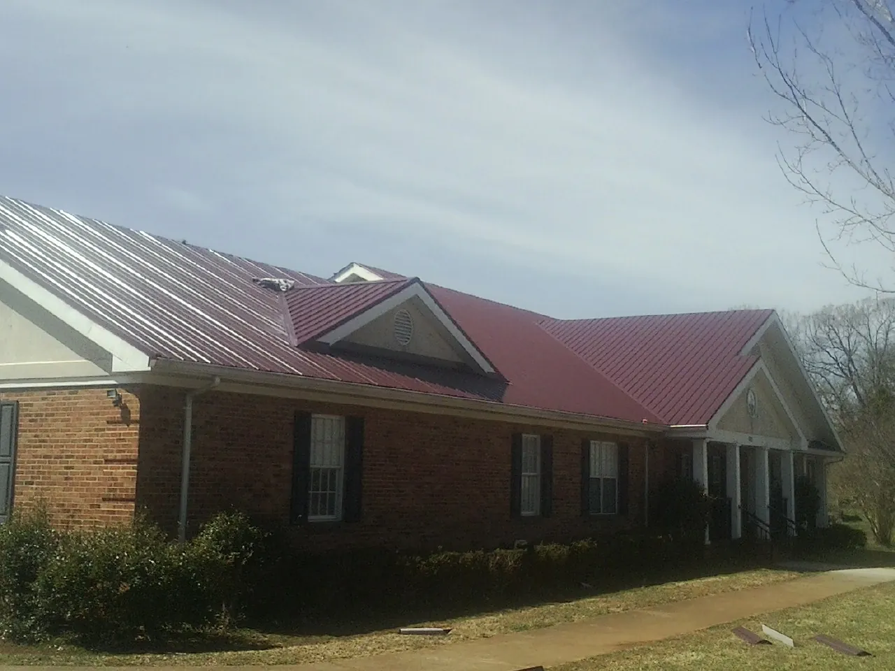 Red metal roof with gabled entries on a long brick building, from a Hail Damage Roof Repair job in Rising Sun
