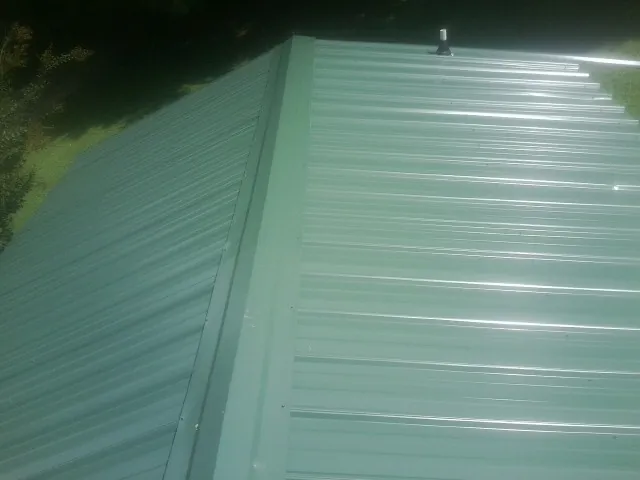 New green metal panels meeting at the ridge of a roof — Flat Roof Repair work by our crew in Rising Sun