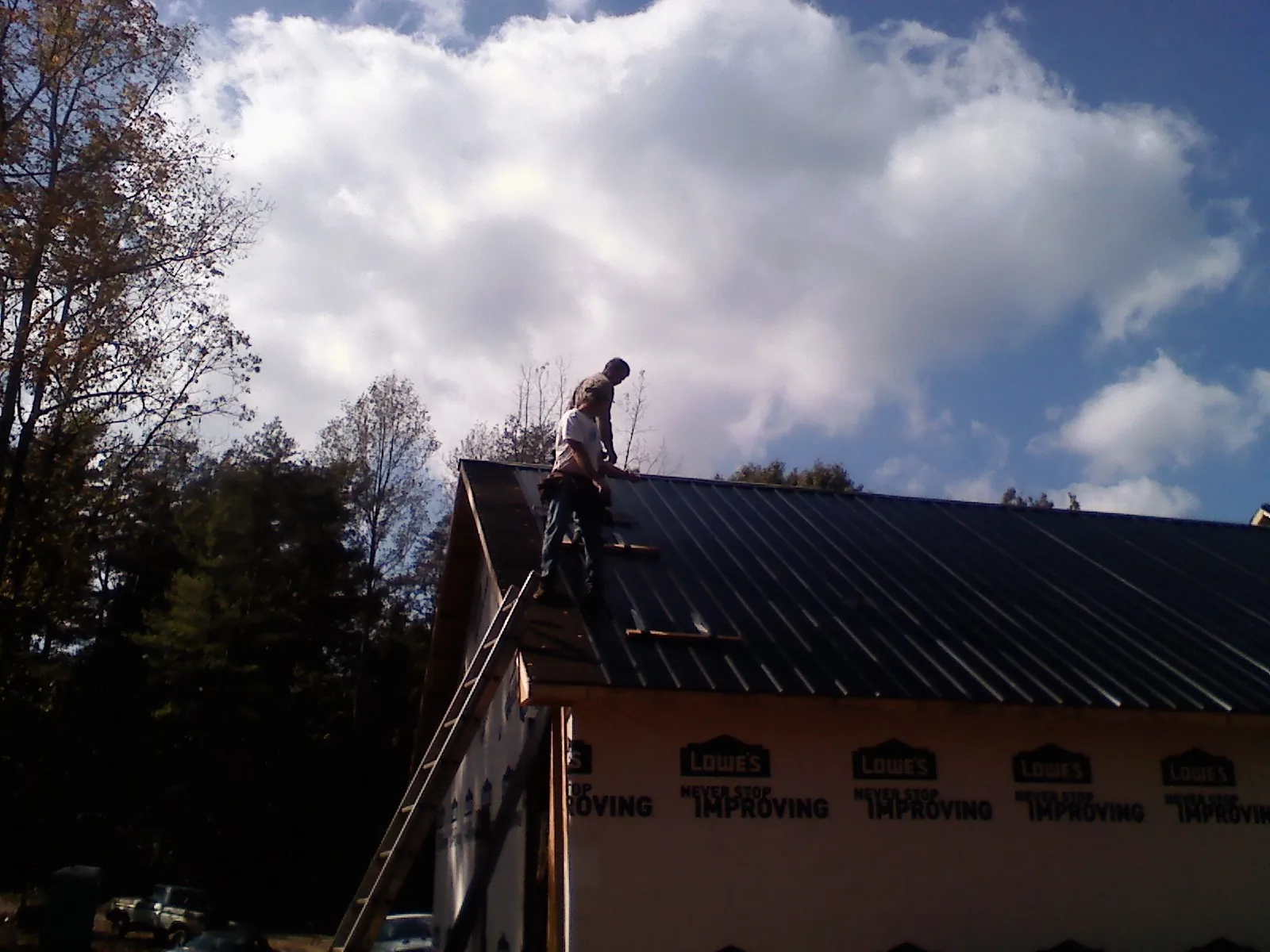Roofer fastening dark metal panels high against a cloudy sky, from a Roof Inspection job in Rising Sun